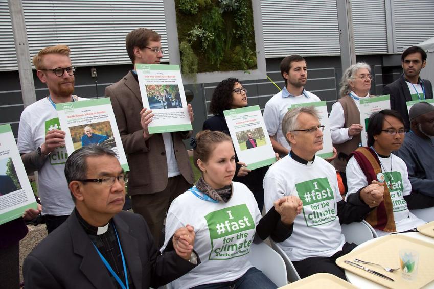 An interfaith group of religious leaders sits in front of empty trays during a public action at COP21 in Paris in 2015. Photo: LWF/Ryan Rodrick Beiler An interfaith group of religious leaders sits in front of empty trays during a public action at COP21 in Paris in 2015. Photo: LWF/Ryan Rodrick Beiler